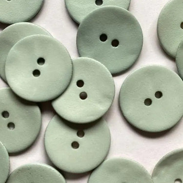 Multiple light green buttons with two holes on a white background
