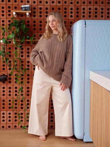 Model wearing cozy sweater leaning against blue fridge for 52 Weeks of Sweaters pre-order