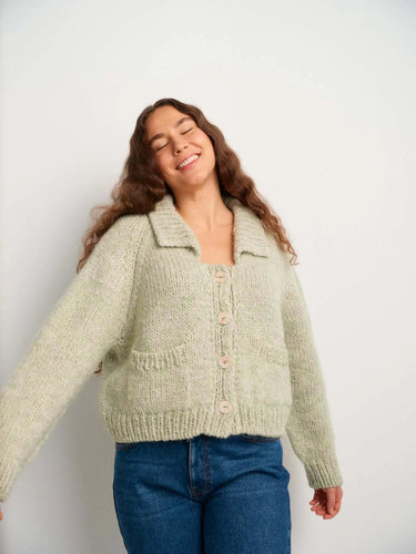 Woman wearing a cozy sweater from the book '52 Weeks of Sweaters', smiling with closed eyes against a white background