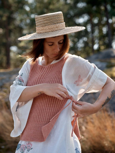 Woman tying a knitted vest, outdoor setting, representing Laine Magazine Spring 28 fashion.