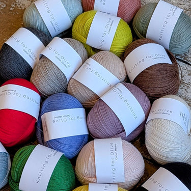 Collection of Knitting for Olive COTTON MERINO yarn balls in various colors on a wooden surface.