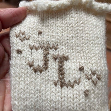 Close-up of knitted fabric showcasing Duplicate Stitch letters, part of Justine Lee's workshop on embellishing knitwear.