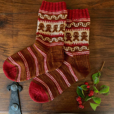 Festive Gift for Knitters: Gingerbread Man Sock Kit with red and brown patterned socks on wooden background with holly.