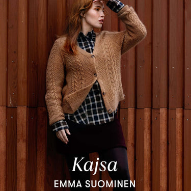 Woman wearing a brown knitted cardigan over a plaid shirt standing against a wooden wall from Archipelago Knitting collection.