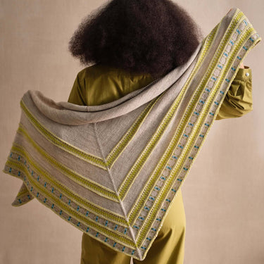 Person showcasing a knitted shawl with Beaded Colourwork design in neutral and green tones.