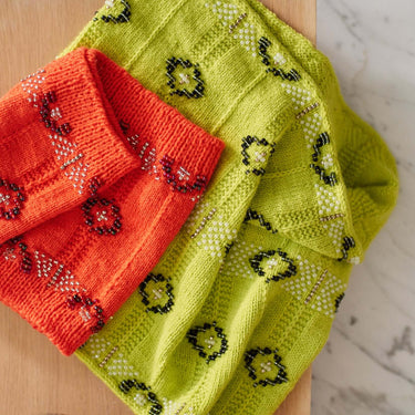 Bright knitted cloths showcasing Beaded Colourwork technique with bold patterns on a wooden surface.