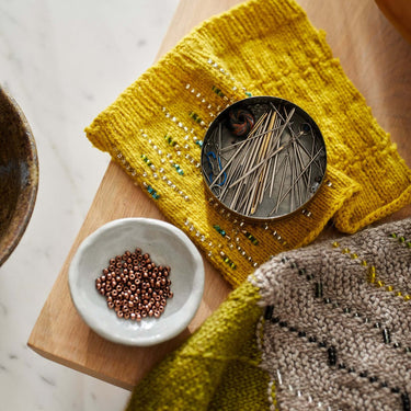 Knitting accessories and beads for Beaded Colourwork projects on a wooden surface