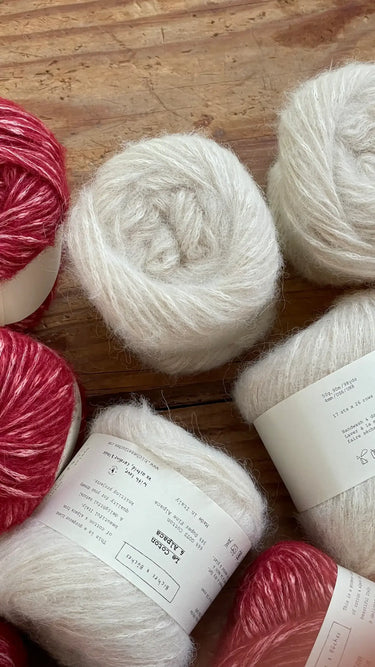 Le Coton & Alpaca yarn in red and white skeins on wooden table.