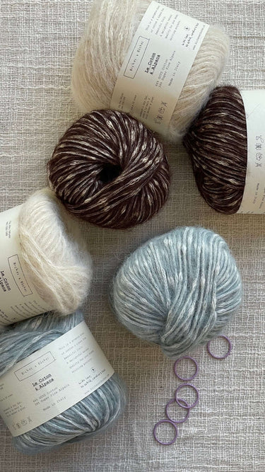 Balls of Le Coton & Alpaca yarn in various colors on a textured background.