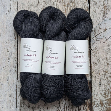 Wool Decanted Vintage 23 4ply Yarn in dark grey, soft British yarn ideal for knitting, displayed on rustic wood background.