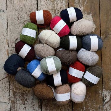 Assorted skeins of Knitting for Olive Heavy Merino wool yarn in various colors on a wooden surface.