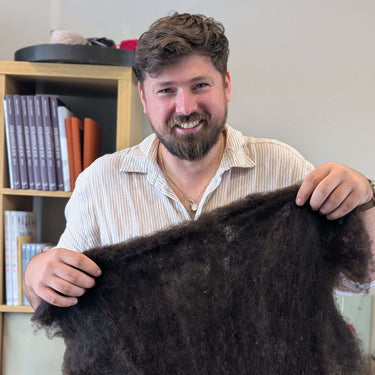 Man holding a large piece of dark wool in an indoor setting