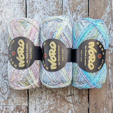 Three skeins of Silk Garden Sock Solo yarn displayed on a wooden surface, showcasing its tweedy shades and luxurious blend of silk, mohair, and wool.