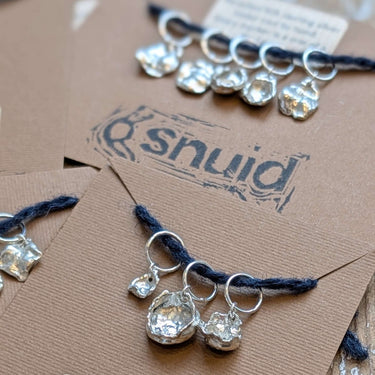 Handcrafted Silver Stitch Markers by Snuid, made from recycled 925 silver, showcasing unique organic shapes on display.