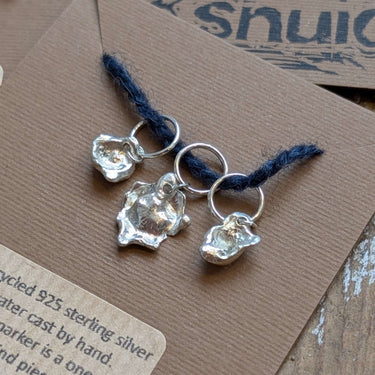 Handcrafted Silver Stitch Markers made from recycled 925 silver, featuring unique water-cast organic shapes, displayed on a brown card.
