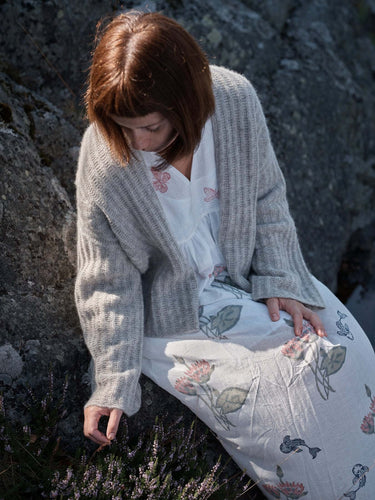 Woman in a cardigan sitting on rocky beach, Laine Magazine Spring Issue 28 theme.