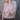 Woman wearing a light pink knitted sweater against a wooden background. Tukubook knitting book