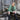 Woman in a green sweater and black rain boots sitting on a wooden platform in front of a rustic wooden building. Tukubook knitting book