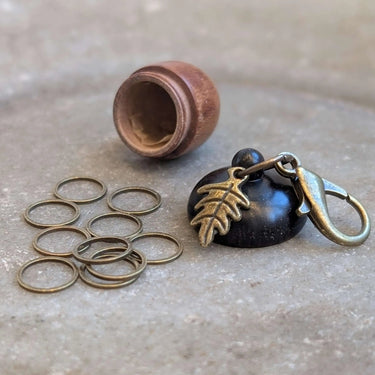 Wooden acorn stitch marker case with open lid, featuring 10 ring stitch markers and a large clasp for easy attachment to knitting bags.