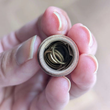 Open wooden acorn case revealing 10 ring stitch markers, held in hand, ideal for knitters' emergency storage and gift.