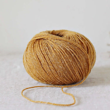 Alice | De Rerum Natura yarn ball in gold with organic Mérinos d'Arles and linen blend, showcasing elasticity and luminous texture. Button included.