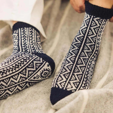 Person wearing intricately patterned socks from the Amirisu Sock Knitting Club collection on a beige knit blanket.