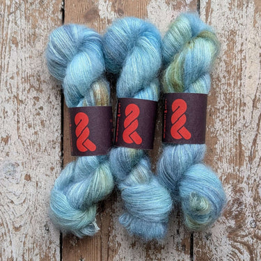A&P Lace Silk Mohair skeins in soft blue and green hues on textured wooden surface.