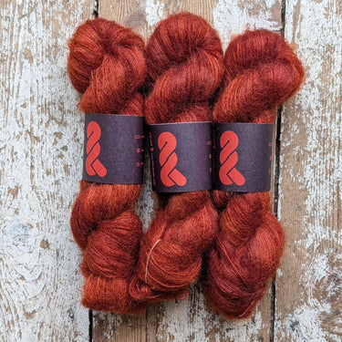 Three skeins of A&P Lace Silk Mohair in rich reddish-orange hues, hand dyed for unique colors and softness.
