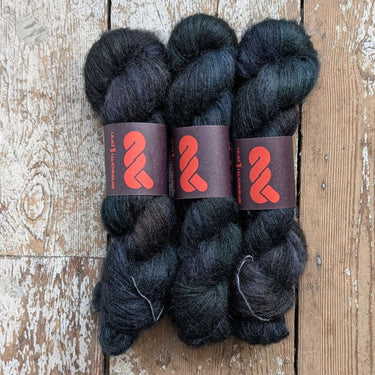 A&P Lace Silk Mohair yarn in dark shades, showcasing its luxurious fluffy texture on a wooden surface.