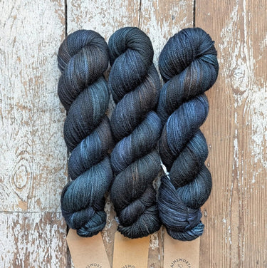 Three skeins of A&P Plump Sock DK yarn on wooden surface, hand dyed in dark tones. Perfect for knitting socks and accessories.