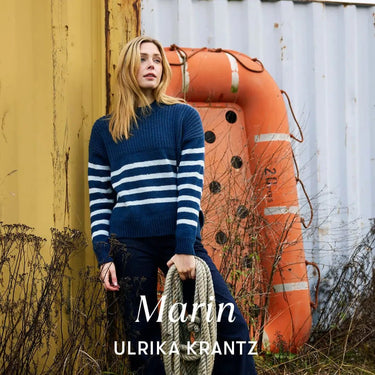 Woman in blue striped sweater for Archipelago Knitting pre-order, holding rope by orange buoy.