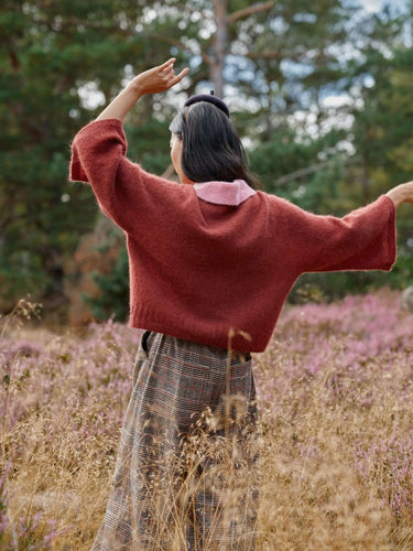 Woman wearing knitwear inspired by the Moomins from Art of the Sea collection by Laine, available for pre-order. Scenic field background.