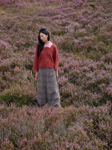 Woman wearing knitwear inspired by Art of the Sea amidst a field of pink heather, pre-order collection by Laine.