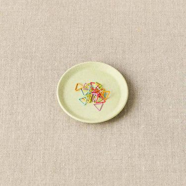 Cocoknits Magnetic Notions Dish holding colorful metal stitch markers on a linen surface.