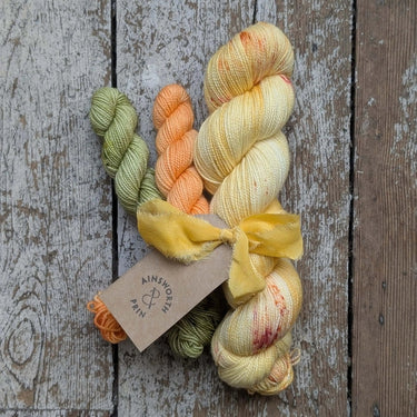 Ainsworth & Prin Flower Yarn Knitting Kits with colorful skeins and silk ribbon on wooden background.