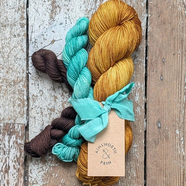 Yarn Knitting kits with skeins in various colors by Ainsworth & Prin, tied with a hand-dyed silk ribbon, perfect for all seasons.