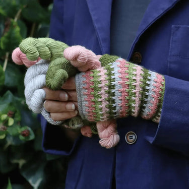 Person holding a Gillyflower Mini Set knitting gift set with colorful skeins and fingerless mitten.