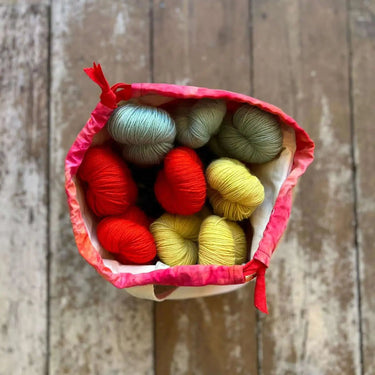 Top view of a vibrant ice dyed Craft Project Bag filled with colorful yarn skeins on a wooden floor.