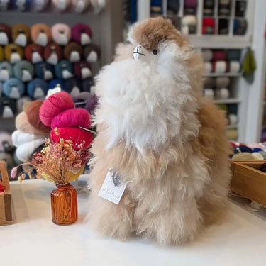 Fluffy Inkari Stuffed Alpaca in store display with colorful yarn background