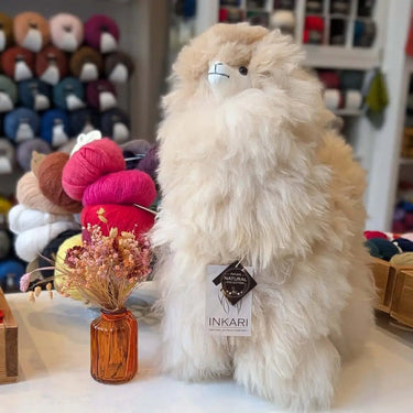 Stuffed Alpaca from Inkari in Natural type, showcasing its fluffy texture and adorable design in a cozy shop setting.