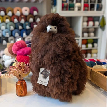 Brown Inkari Stuffed Alpaca in a yarn shop setting. Adorable and soft, part of the Natural series. Focus keyword: Stuffed Alpaca.