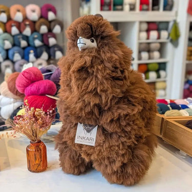Large Natural Inkari Stuffed Alpaca animal in a cozy shop setting, featuring soft brown fur and a charming expression.