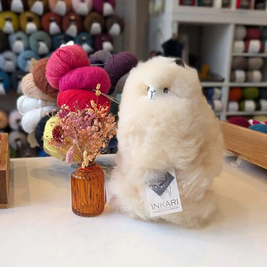 Inkari Stuffed Alpaca animal on display with colorful yarns and a small vase.