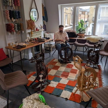 Instructor leading a Yarn Spinning class with spinning wheels and wool in a cozy studio setting.
