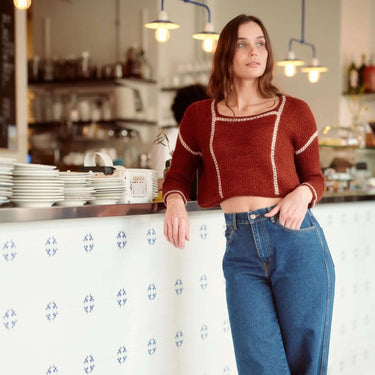 Woman in a red sweater and blue jeans standing in a cafe.