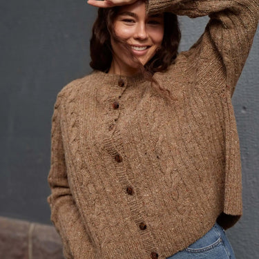 Woman wearing a brown knitted sweater against a gray wall.