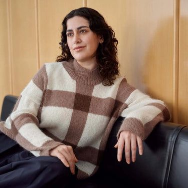 Woman wearing a checkered knit sweater from Laine Magazine Issue 27, sitting on couch.