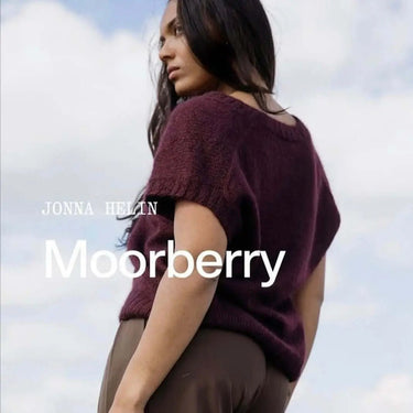 Woman wearing a maroon sweater with 'Moorberry' text against a cloudy sky
