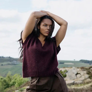 Woman wearing a maroon sweater and brown pants with a scenic background