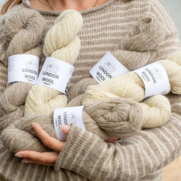 Woman holding skeins of London Wool from London City Farm Yarn Project, showcasing blend of rare sheep fleeces, in neutral tones.